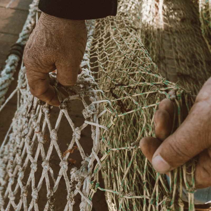 Manos curtidas de un pescador remendando una red.