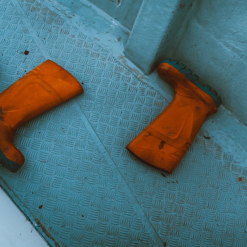 Un par de botas de goma naranjas sobre la cubierta azul del barco.