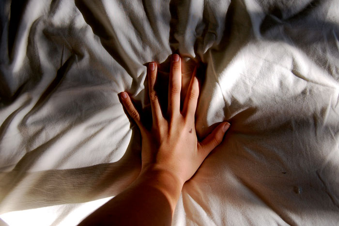 Una solitaria mano sobre las sábanas, con un pequeño corazón tatuado.